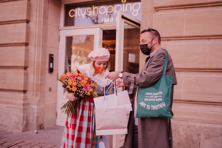 Couple devant le Cityshopping Infopoint avec sacs de shopping et bouquet de fleurs à la main